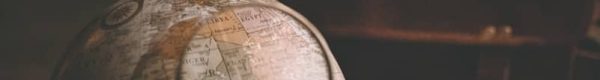 person holding magnifying glass near desk globe